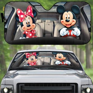 May include: A black car sunshade featuring Mickey Mouse and Minnie Mouse. Mickey is at the wheel, and Minnie is in the passenger seat. Both characters are smiling. The sunshade is installed in a car.