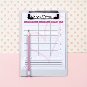 May include: A white clipboard with a pink heart design and the text "Assignment Tracker" at the top. The clipboard has columns labeled "Assignment", "Teacher", "Due Date", and "Done". There are checkboxes next to each row. A pink pencil is lying on the clipboard.
