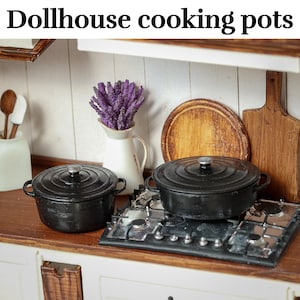 Könnte beinhalten: Miniatur-Kochtopf-Sets aus schwarzem Gusseisen mit Deckeln auf einem Puppenhaus-Herd. Das Bild enthält eine weiße Kanne mit lila Blumen, Holzschneidebretter und den Text "Dollhouse cooking pots".