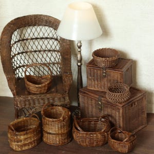 Könnte beinhalten: Eine Sammlung von braunen, geflochtenen Miniatur-Weidenkörben und Truhen, die um einen kleinen Weidenstuhl und eine Lampe angeordnet sind. Das Set enthält verschiedene runde und ovale Körbe, zwei rechteckige Truhen mit Deckel und einen hohen Stuhl.