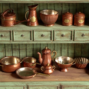 May include: Miniature copper kitchenware set displayed on a green cabinet. The collection includes a teapot, pans, bowls, and jars. The copper items have a shiny finish, and the cabinet has a distressed, vintage appearance.