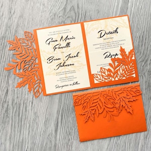 May include: Orange wedding invitation with a laser cut design of autumn leaves. The invitation reads "You are joyfully invited to celebrate the wedding of Gina Marie Fanelli and Bean Jacob Johnson. Sunday, September 18, 2022 at 3:00pm in the afternoon. Chota Falls Estate 1800 Hickman Airfield Road Clayton, Georgia. Reception to follow." The details card reads "Details Reception Immediately following the Holy Sacrifice of the Mass, we will have cocktail hour, dinner, and dancing at the Chota Falls Estate. Drop"