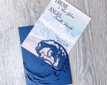 May include: A blue wedding invitation with a wave cut-out design. The invitation features a watercolor background with a beach scene and the text "Irene Am Gelinas Angel Carvalho Mendes" and "Invite you to their wedding ceremony".