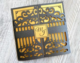 May include: Black and gold wedding invitation with a laser cut design of a gate. The invitation has a gold background with black lettering and a black band around the middle. The initials "M & J" are in a gold square in the center of the invitation.