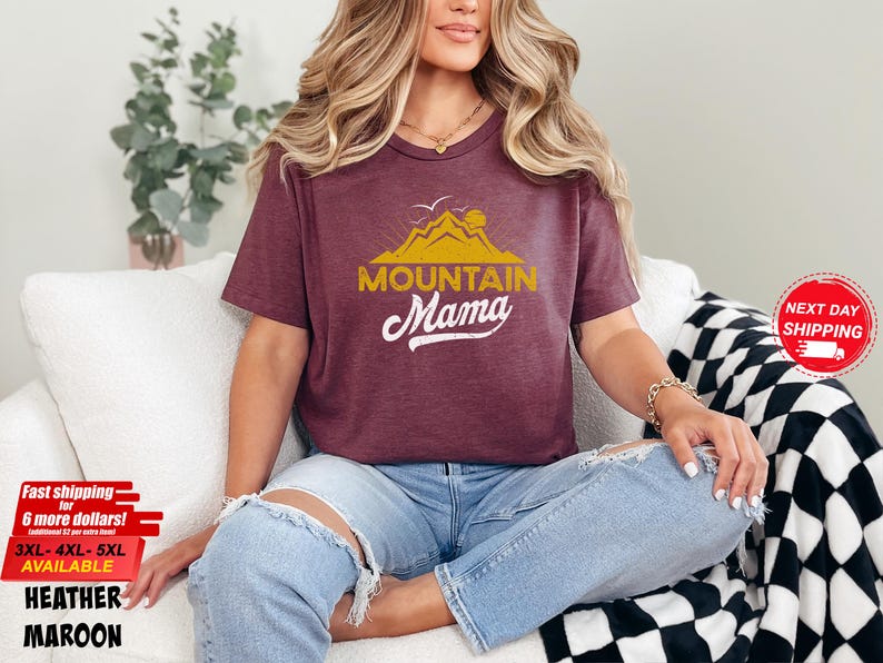 May include: Maroon heather t-shirt with the text "Mountain Mama" in gold and white. The shirt features a mountain and sun graphic. Available in sizes 3XL, 4XL, and 5XL. Fast shipping is available.