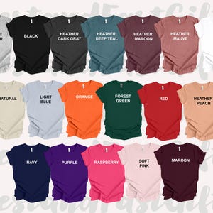 May include: A collection of short-sleeved t-shirts in various colors, including black, white, and heather gray. Each shirt has a different color name printed on it, such as "Orange," "Navy," and "Maroon." The shirts are neatly arranged, showcasing a variety of options.
