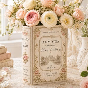 May include: A rectangular book-shaped vase in cream with floral borders, featuring the text A LOVE STORY, WRITTEN BY Eleanor & Henry, EST 08.16.2026, IN EVERY CHAPTER, I CHOOSE YOU, and FOREVER, MOST DEVOTEDLY, filled with pink and white roses.