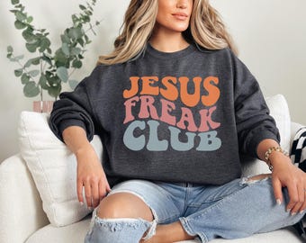 Puede incluir: Una sudadera gris oscuro con el texto "JESUS FREAK CLUB" en una fuente retro y colorida. El texto está en tonos naranja, rosa y azul.
