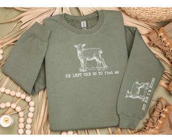 Può includere: Felpa verde con un'illustrazione di agnello bianco e il testo "He left the 99 to find me" sul davanti. La manica sinistra ha un'illustrazione di agnello bianco e il testo "But now I'm found".
