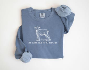 Può includere: Una felpa blu con una grafica bianca di un agnello e il testo "HE LEFT THE 99 TO FIND ME".
