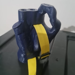 Pode incluir: Uma mão azul impressa em 3D com uma alça amarela. A mão tem dois furos no topo e uma alça lateral. A alça é ajustável com uma fivela.