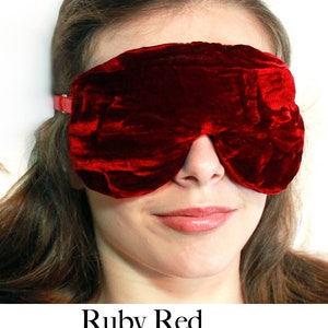 May include: A close-up of a woman wearing a ruby red velvet sleep mask. The mask covers her eyes and is secured with an elastic band.