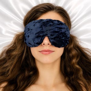 May include: A dark navy blue velvet sleep mask with a textured, crushed finish. The mask is contoured to fit over the eyes and nose, featuring a soft, plush fabric construction that provides full coverage for light blocking during rest or sleep.