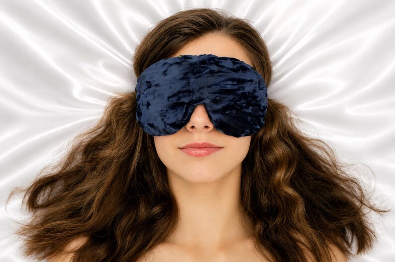 May include: A dark navy blue velvet sleep mask with a textured, crushed finish. The mask is contoured to fit over the eyes and nose, featuring a soft, plush fabric construction that provides full coverage for light blocking during rest or sleep.
