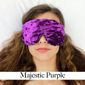 K&ouml;nnte beinhalten: Eine Schlafmaske aus violettem Samt mit einer geknitterten Textur. Die Maske wird von einer Person mit langen braunen Haaren getragen.