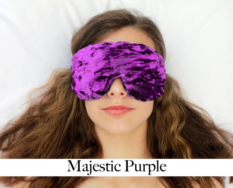 K&ouml;nnte beinhalten: Eine Schlafmaske aus violettem Samt mit einer geknitterten Textur. Die Maske wird von einer Person mit langen braunen Haaren getragen.