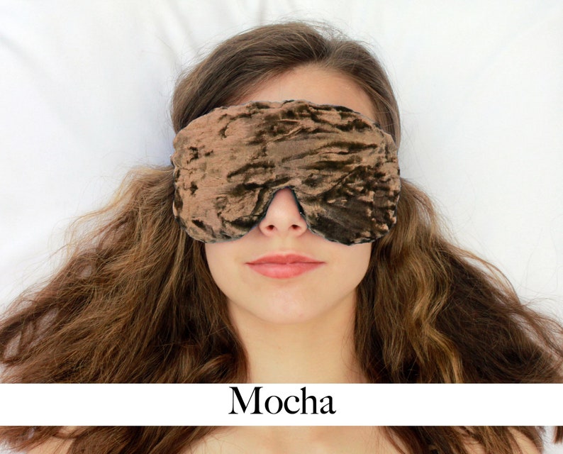 K&ouml;nnte beinhalten: Eine braune Schlafmaske aus Samt mit einem dezenten Schimmer. Die Maske wird von einer Person mit langen braunen Haaren getragen, die auf einer wei&szlig;en Oberfl&auml;che liegt. Das Wort "Mocha" steht unter dem Bild.