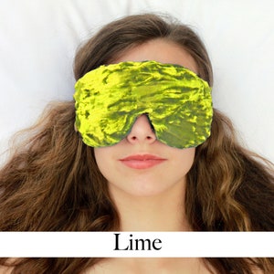 K&ouml;nnte beinhalten: Eine Schlafmaske aus weichem Samt in Limettengr&uuml;n. Die Maske wird von einer Person getragen, die auf einem wei&szlig;en Bett liegt.