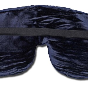 May include: A dark navy blue velvet sleep mask featuring a soft, plush texture and a contoured shape. The mask includes a wide, black elasticated strap that stretches horizontally across the back, secured with silver-toned metal adjusters on both ends.