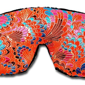 May include: An eye mask featuring a bright orange fabric with a detailed floral design in pink, blue, and brown. The mask has a black trim and is designed to block out light.