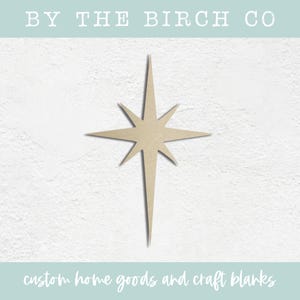 May include: A wooden cutout of a large, eight-pointed star in a light brown color. The star is a simple design with straight lines and a pointed tip.