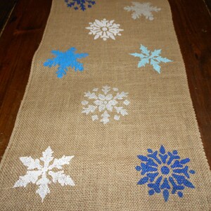May include: A burlap table runner with a winter theme featuring blue and white snowflake designs.