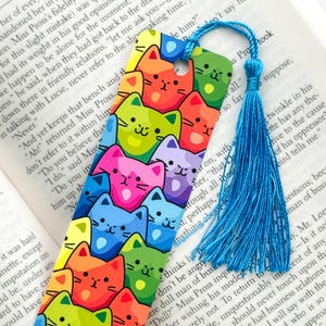 May include: A colorful bookmark featuring a repeating pattern of cartoon cats with rainbow-colored fur. The bookmark has a blue tassel.
