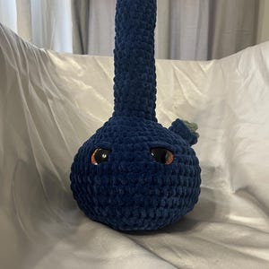 May include: A blue crocheted bong with orange and green accents. The bong has two large black eyes.