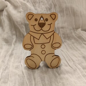 Puede incluir: Un adorno de madera en forma de oso con un diseño sencillo. El oso es marrón y tiene una cara sonriente. Es una decoración linda y caprichosa para una habitación de niños o una guardería.