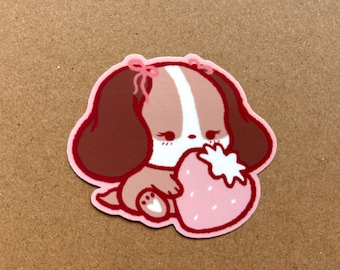 May include: A sticker featuring a cartoon dog with brown ears and a white stripe on its head, wearing a pink bow. The dog is holding a pink strawberry. The sticker has a pink outline.