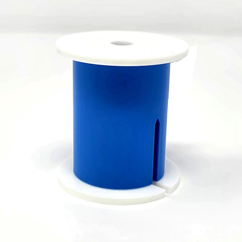 May include: A blue and white spool-shaped object. The cylindrical body is a vibrant blue, with a vertical slit. The top and bottom are white, circular discs. The top disc has a small hole in the center.