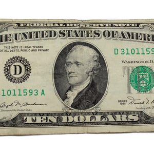 May include: A United States ten-dollar bill featuring a portrait of Alexander Hamilton. The bill is primarily green and black, with the text "THE UNITED STATES OF AMERICA" and the number "10" prominently displayed.