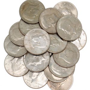 May include: A pile of silver half-dollar coins, featuring the profile of a person and the inscriptions "IN GOD WE TRUST" and the year 1976. The coins are scattered against a white background.