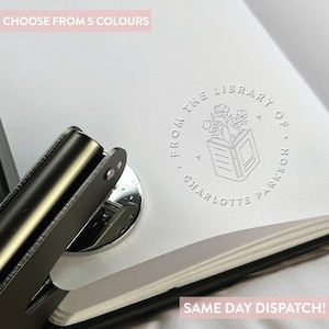 May include: A white self-inking stamp with a round design featuring a book with flowers coming out of the top. The text reads "From the Library of Charlotte Parkinson".