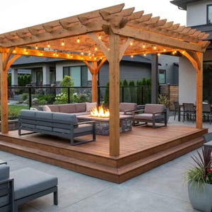 May include: A wooden pergola structure with a lattice roof and string lights, positioned over a raised deck. The deck features a stone fire pit with active flames, a gray sectional sofa, and two matching armchairs with gray cushions.