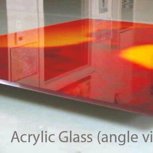 K&ouml;nnte beinhalten: Eine rote und orangefarbene Acrylglasscheibe mit einem verschwommenen Bild einer Personensilhouette. Die Scheibe ist schr&auml;g gestellt und scheint auf einer Glasoberfl&auml;che zu liegen.