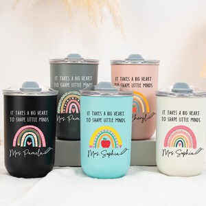 May include: Five cylindrical tumblers with lids in black, dark gray, light blue, pink, and white. Each features a rainbow graphic, a pencil, and the text "It takes a big heart to shape little minds" along with a personalized name in script font.