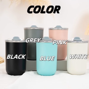 May include: Five cylindrical tumblers with lids, labeled with the text COLOR, BLACK, GREY, BLUE, PINK, and WHITE. The tumblers are available in matte black, dark grey, light blue, soft pink, and white, each featuring a clear lid with a grey stopper.