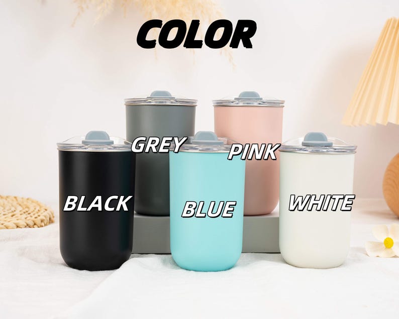May include: Five cylindrical tumblers with lids, labeled with the text COLOR, BLACK, GREY, BLUE, PINK, and WHITE. The tumblers are available in matte black, dark grey, light blue, soft pink, and white, each featuring a clear lid with a grey stopper.