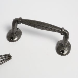 May include: A dark gray metal cabinet pull with a textured finish. The pull has a curved handle and two oval-shaped mounting plates. Four screws are included for installation. Hardware for furniture.