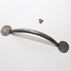 Puede incluir: Un tirador de metal curvado con dos placas de montaje circulares y tres tornillos. El tirador es de color gris oscuro y tiene una superficie texturizada, lo que sugiere un aspecto envejecido. Ideal para herrajes de muebles o armarios.