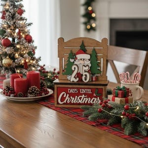 May include: A wooden Christmas countdown calendar with a Santa Claus design, displaying "25 Days Until Christmas." The scene includes a small Christmas tree, red candles, and festive decorations on a wooden table.