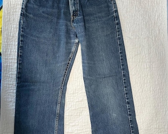 May include: A pair of blue denim jeans with a classic five-pocket design. The jeans have a straight leg cut and a button and zipper closure. The denim has a faded appearance, suggesting wear. The jeans are laid flat on a white surface.