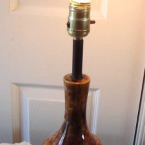 May include: A brown and gold ceramic table lamp with a white light bulb. The lamp has a bulbous base and a black metal stem.