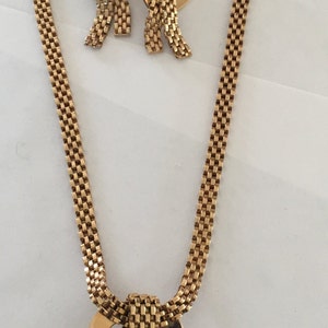May include: A gold tone necklace and earrings set with a heart-shaped pendant and matching heart-shaped earrings. The necklace and earrings are made of a chain link design.