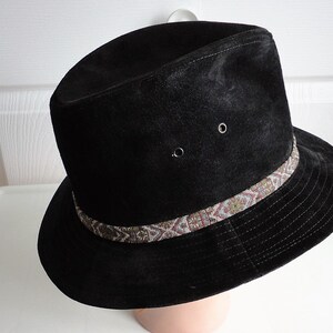 May include: A black suede fedora hat with a brown and white patterned band.
