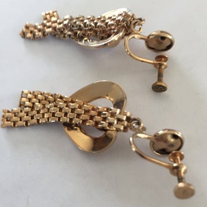 May include: A pair of gold tone clip-on earrings with a heart-shaped design and a dangling chain.