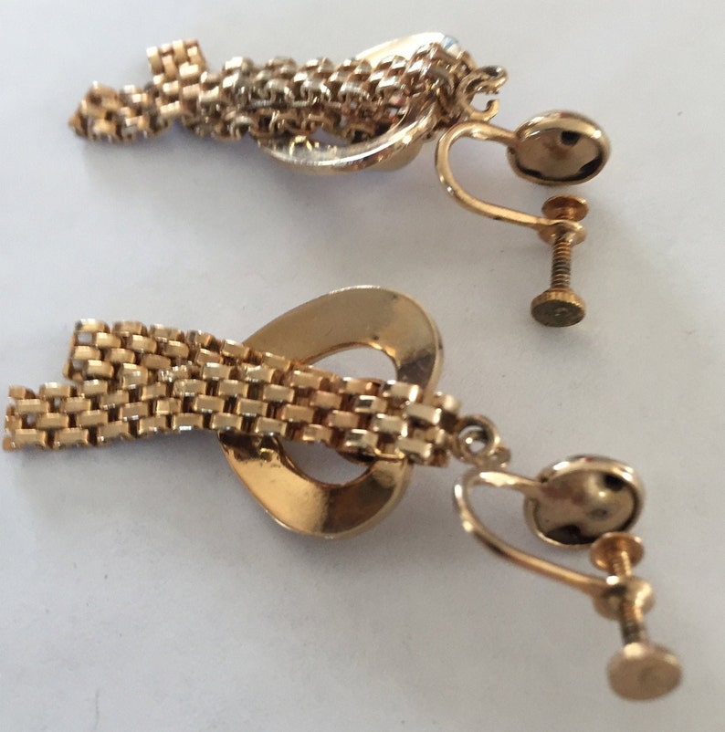 May include: A pair of gold tone clip-on earrings with a heart-shaped design and a dangling chain.