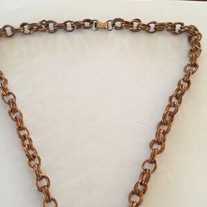 May include: A copper-toned necklace with a double-link chain design. The necklace features a gold-colored clasp. The chain is made of small, interconnected oval links, creating a textured appearance. The necklace is displayed against a white background.