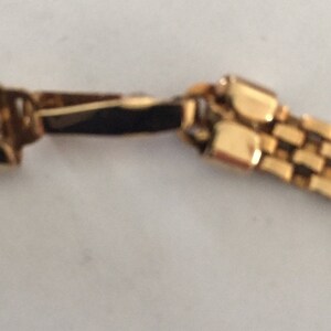 May include: A gold chain bracelet with a box clasp. The chain is made of small, square links.